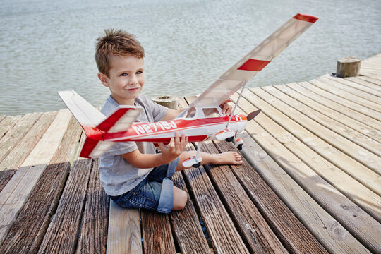 Smiling cute boy playing with airplane toy on pier