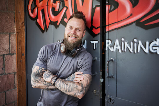 Smiling male fitness instructor leaning on door outside gym