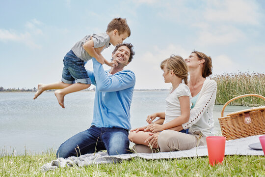 Man playing with boy while sitting by girl and woman on blanket