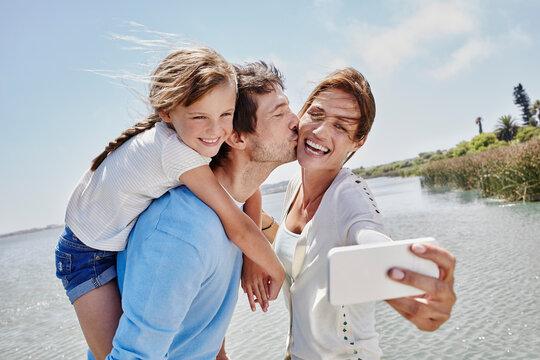 Cheerful family taking selfie through mobile phone by lake