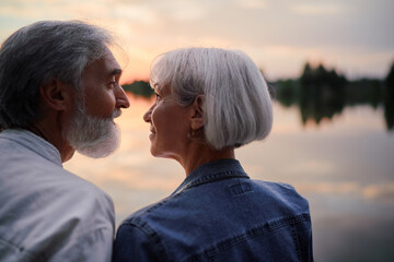 Romantic holiday. Senior loving couple sitting together on lake bank enjoying beautiful sunset.