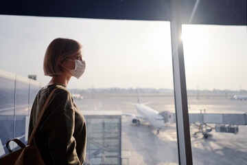 Young woman with a backpack wearing an anti-virus mask on her face at the airport.