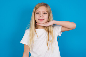 beautiful Caucasian little girl wearing white T-shirt over blue background cutting throat with hand...