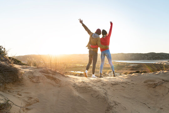 Young Couple Standing With Hand Raised And Arm Around On Each Other Against Sky