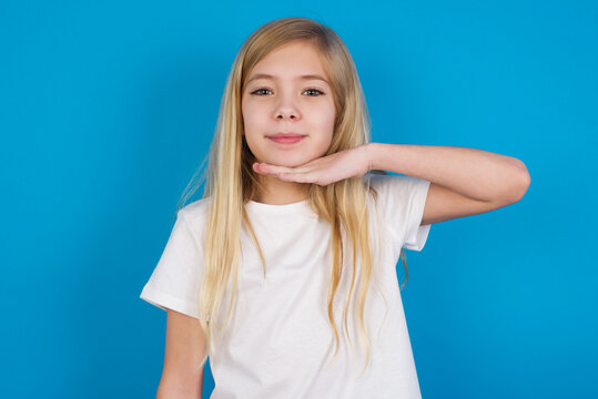 beautiful Caucasian little girl wearing white T-shirt over blue background cutting throat with hand as knife, threaten aggression with furious violence.