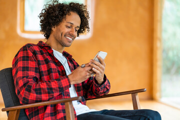 Young man using smart phone while sitting on armchair at spacious room