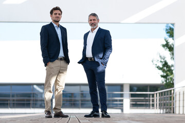 Business people smiling while standing with hands in pockets at office terrace