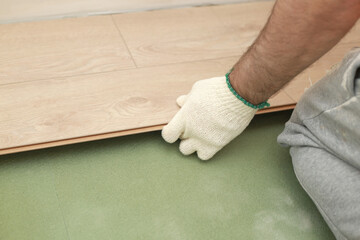 Installing laminate or parquet floor in room, detail on man hands fitting wooden tile, over green foam base