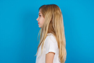 Profile portrait of nice beautiful Caucasian little girl wearing white T-shirt over blue background...