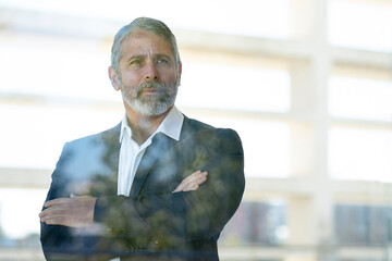 Mature entrepreneur looking away while standing with arms crossed in office
