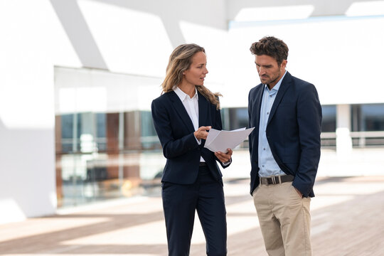 Businesswoman explaining paper while standing by colleague at office building terrace
