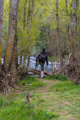 Teenager with fishing suit, rod and tools crossing some branches of the trees to go to the river to catch trout and other fish to enjoy an afternoon