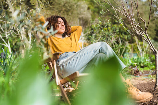 Woman with hands behind head relaxing on deck chair in garden