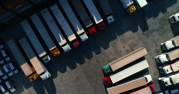 Aerial view of a semi trucks with cargo trailers standing on warehouses ramps for loading and unloading goods on the big logistics park with loading hub