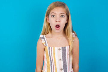 beautiful Caucasian little girl wearing stripped dress over blue background having stunned and...