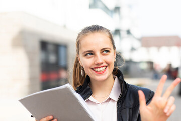 Portrait of young blonde woman standing outdoors with note pad in hand