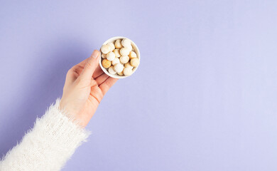 Fototapeta na wymiar The hand of a young girl in a white fluffy sweater holds a plate with traditional dry kurut cheese on a purple background copy space for text