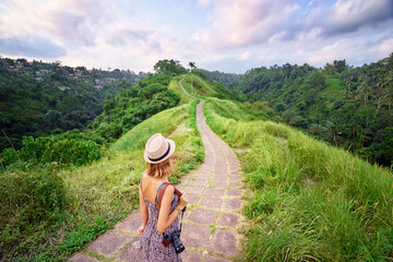 Tourism and travel. Young woman in hat with camera walking on path in Ubud, Bali.