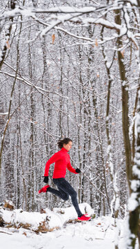 Female sportsperson running over snow covered fallen tree during winter