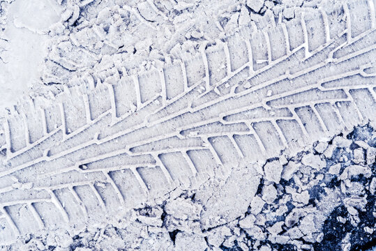Diagonal traces of car tires in the snow on the asphalt. Close up view from above
