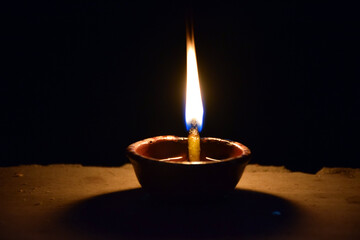 Close up image of a lit clay diya or lamp on floor on Diwali - an Indian hindu festival of lights isolated on black background., Selective focus