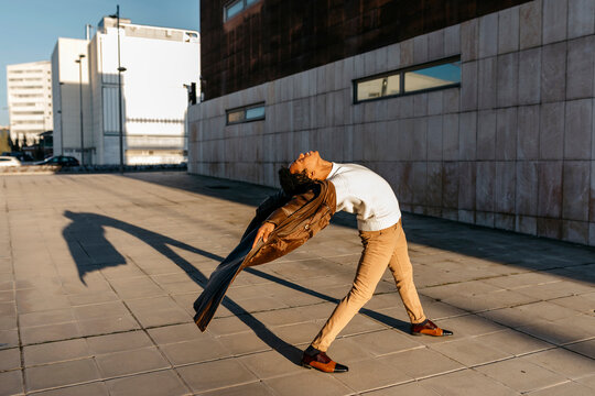 Male dancer practicing dance on footpath against building during sunset