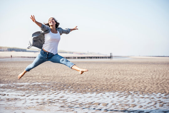 Cheerful young woman jumping over wet sand on sunny day