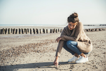 Beautiful woman drawing heart on sand against sky at beach