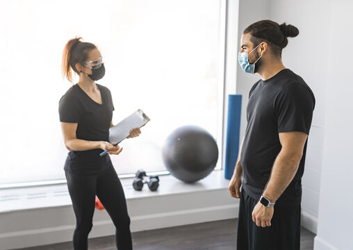 Trainer And Client Discussing Her Progress At The Gym With Mask