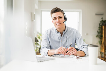 Male professional wearing headset sitting with laptop at desk