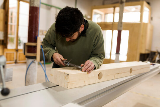 Male carpenter measuring wood with vernier calliper in workshop