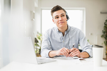 Thoughtful businessman wearing headset looking away while sitting in home office