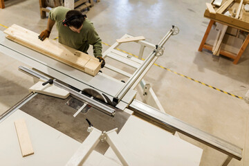 Young male carpenter working at table saw in workshop