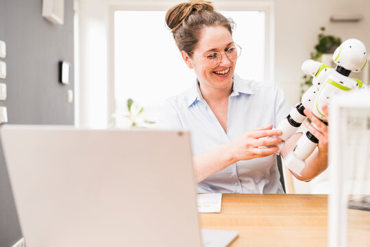 Happy female engineer holding robot while sitting at desk
