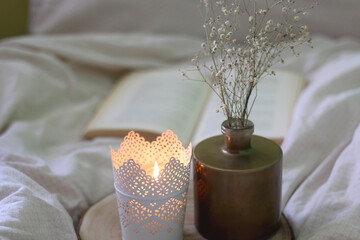Lit candle, vase with gypsophila flowers and open book at home. Selective focus.