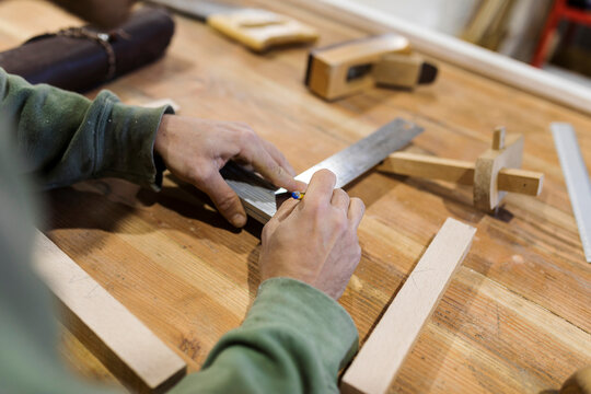 Male carpenter measuring wood material on table in workshop