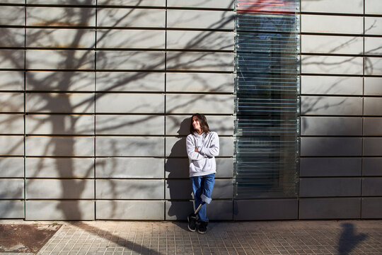 Disabled man with arms crossed standing against wall with tree shadow