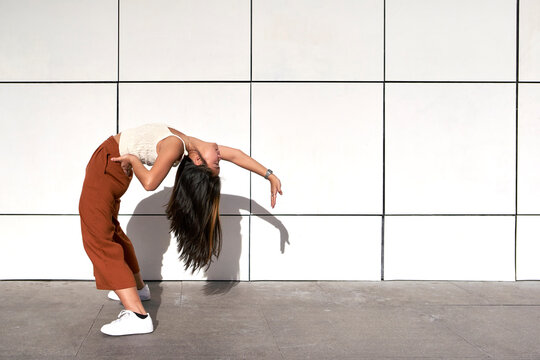 Young woman bending backwards with hand on hip against wall during sunny day
