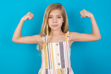 Beautiful Caucasian little girl wearing stripped dress raises arms to show muscles feels confident...