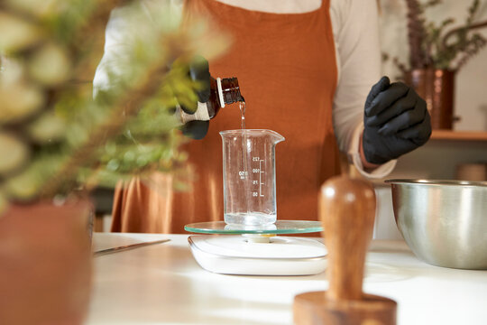 Woman pouring water in glass beaker while making soap in workshop