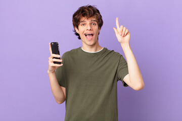 young man holding a cell feeling like a happy and excited genius after realizing an idea