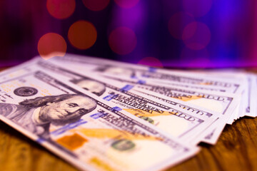Many one hundred dollar bills on purple background with bokeh. Theme of cash settlement in brothel or casino. USD money in macro photography in pink lighting. Side with image of President Franklin.