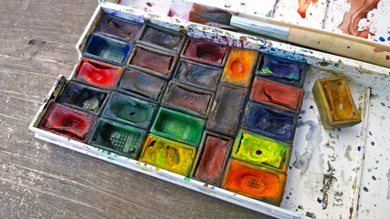 Watercolors and brushes in a dirty box on a wooden background