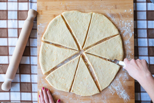 Woman making slices on dough with cutter to make croissants in kitchen