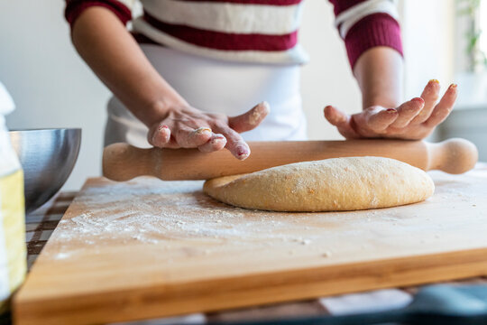 Woman preparing dough with rolling pin to make croissants in kitchen