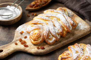 Sweet bun with cottage cheese and raisins on a serving board on a brown wooden table closeup. The concept of home-made high-calorie pastries