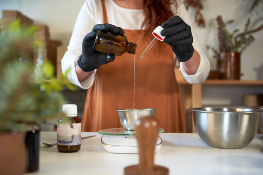 Woman measuring essential oil while making soap in workshop