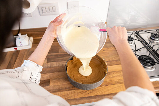 Woman pouring cheesecake filling on crumbled biscuits dough