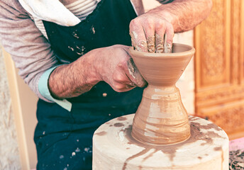 Old pottery master sculpting clay crockery by his hands. Selective focus closeup