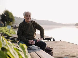 Smiling man drinking coffee while sitting on bench